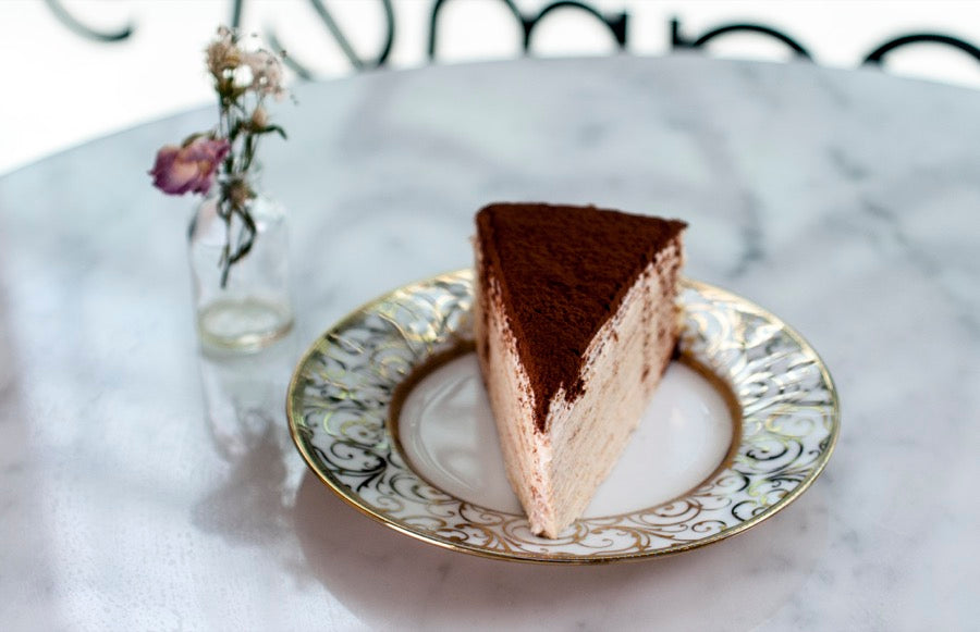 Tiramisu crepe cake slice dusted with cocoa on a gold plate
